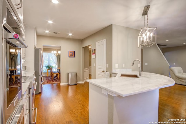 kitchen with a chandelier, a sink, white cabinets, freestanding refrigerator, and wood finished floors