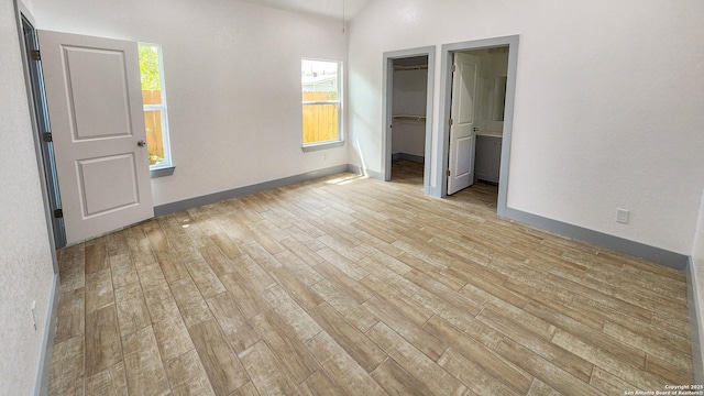 unfurnished bedroom with light wood-style floors, multiple windows, a walk in closet, and baseboards