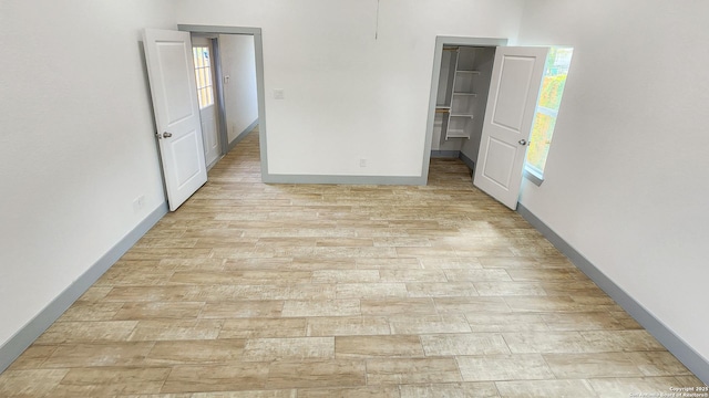 unfurnished bedroom featuring light wood-type flooring, a spacious closet, and baseboards
