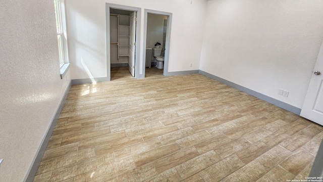 unfurnished bedroom featuring light wood-style floors, a spacious closet, baseboards, and a textured wall
