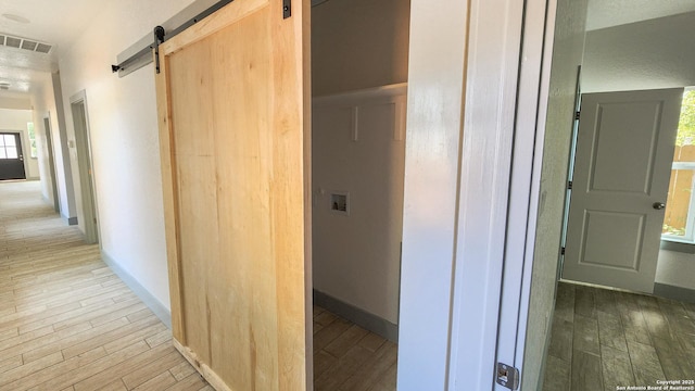 corridor featuring a barn door, light wood-style flooring, and baseboards