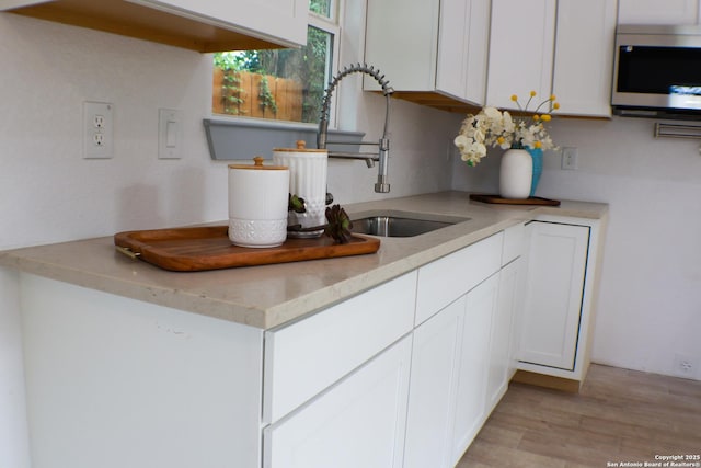 kitchen featuring stainless steel microwave, light wood-type flooring, white cabinetry, a sink, and light countertops