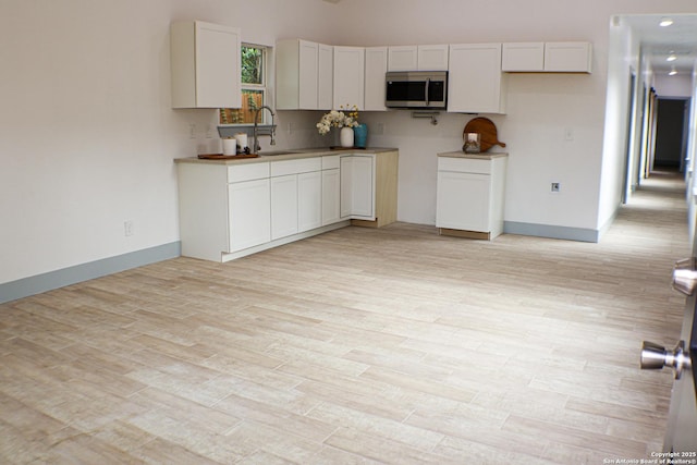 kitchen featuring stainless steel microwave, a sink, light wood-style floors, and white cabinetry