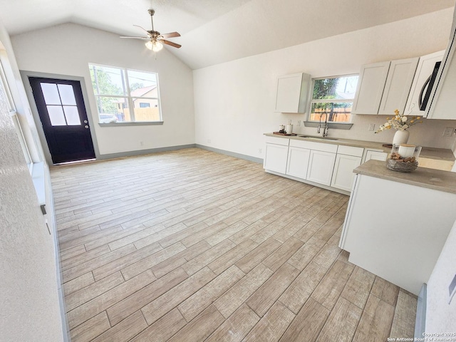 kitchen with a ceiling fan, a sink, light wood-style flooring, white cabinetry, and lofted ceiling