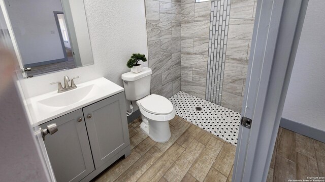 bathroom featuring a tile shower, vanity, toilet, wood finished floors, and a textured wall