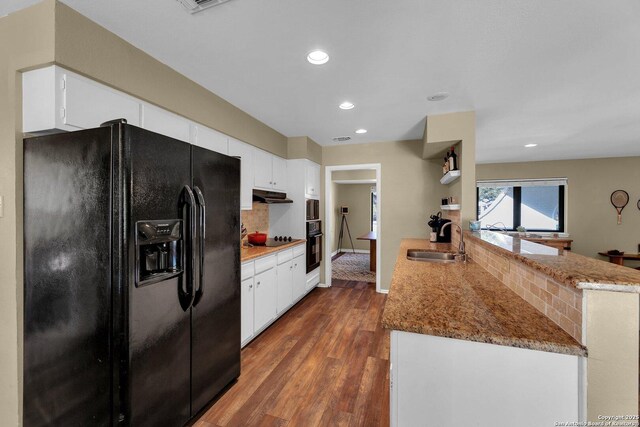 kitchen with black appliances, a sink, under cabinet range hood, dark wood finished floors, and a peninsula