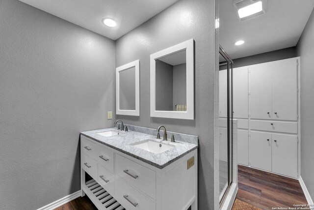 full bath with a textured wall, wood finished floors, double vanity, baseboards, and a stall shower