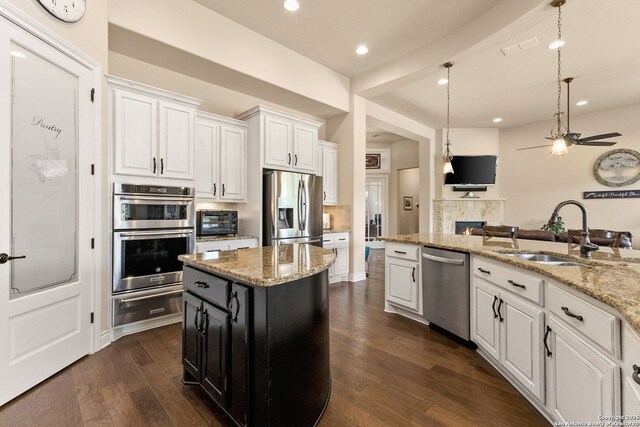 kitchen with a warming drawer, a sink, appliances with stainless steel finishes, a tile fireplace, and white cabinetry