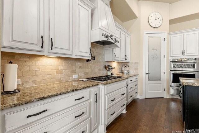kitchen featuring white cabinets, dark wood finished floors, custom exhaust hood, appliances with stainless steel finishes, and light stone countertops