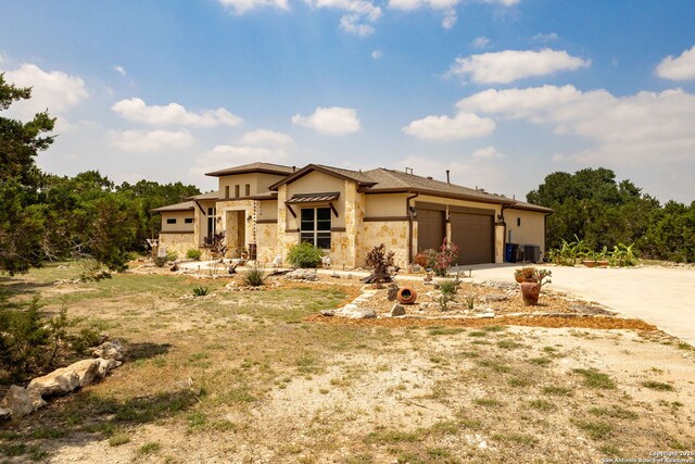 view of front of home featuring an attached garage, stucco siding, stone siding, driveway, and central AC