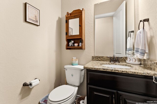 half bath featuring toilet, vanity, and a textured wall