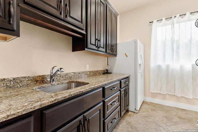 kitchen with a sink, dark brown cabinetry, light stone countertops, and freestanding refrigerator