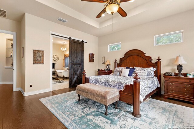bedroom with a barn door, wood finished floors, baseboards, a raised ceiling, and connected bathroom