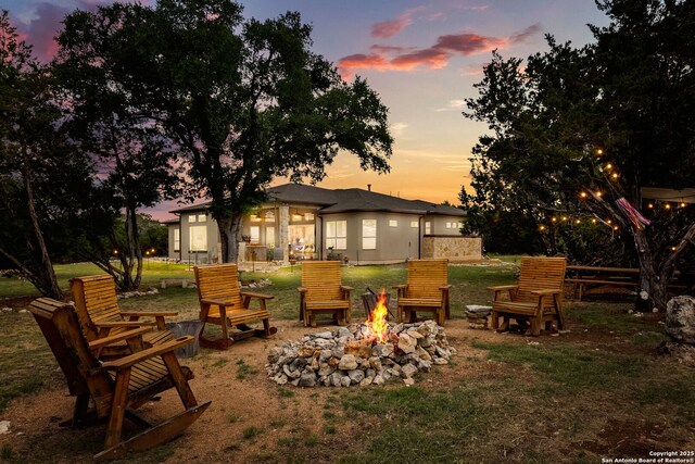 back of property at dusk featuring an outdoor fire pit and a yard