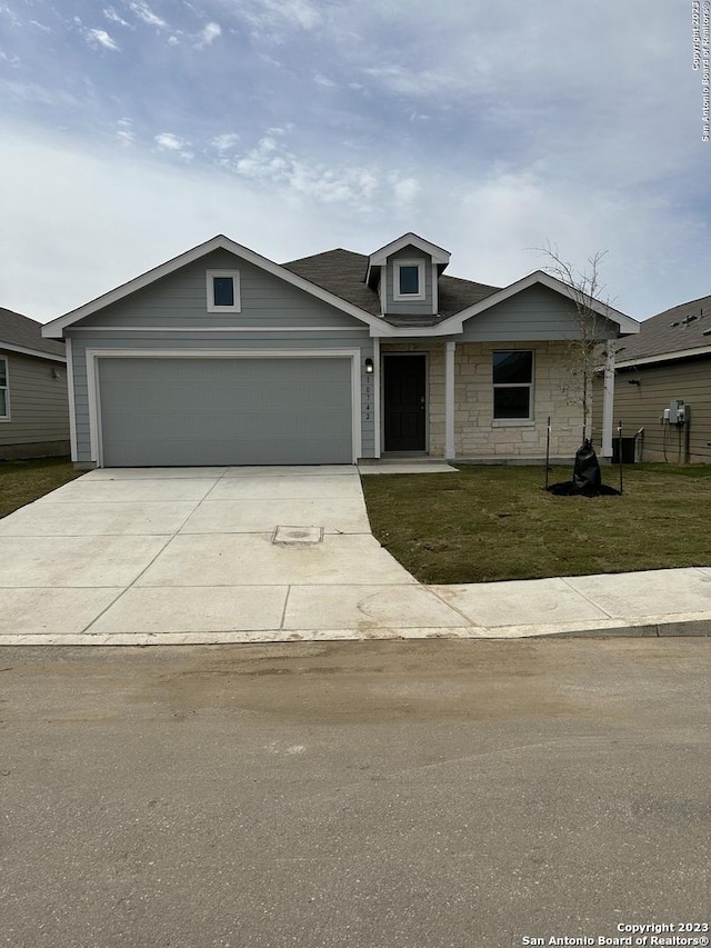 view of front of property featuring an attached garage, driveway, a front yard, and stone siding