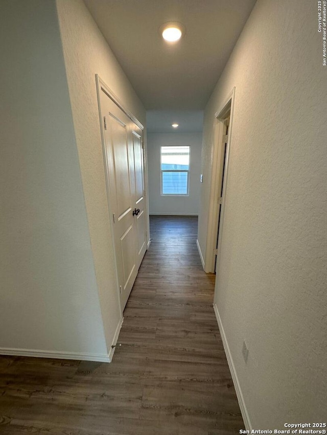 corridor featuring dark wood-style floors, baseboards, a textured wall, and recessed lighting