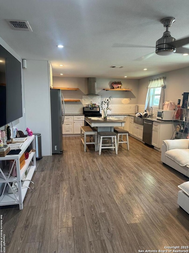 kitchen featuring stainless steel appliances, wall chimney exhaust hood, open shelves, dark wood-style flooring, and white cabinets