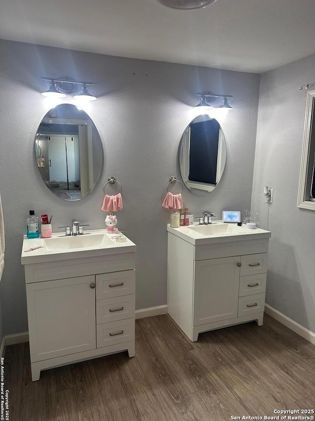bathroom with wood finished floors, baseboards, and two vanities