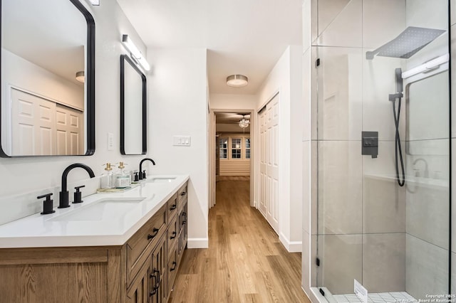 bathroom featuring wood finished floors, a stall shower, baseboards, ceiling fan, and double vanity