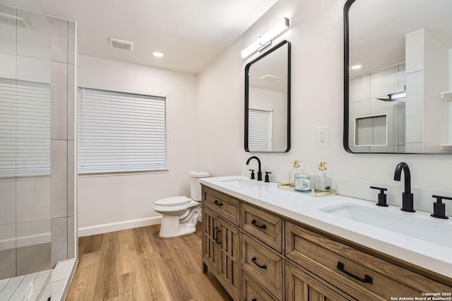 bathroom featuring toilet, wood finished floors, a shower, double vanity, and baseboards