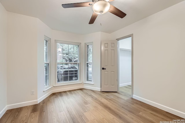 spare room with baseboards, light wood-type flooring, and a ceiling fan