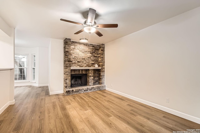 unfurnished living room with a fireplace, a ceiling fan, light wood-style floors, and baseboards