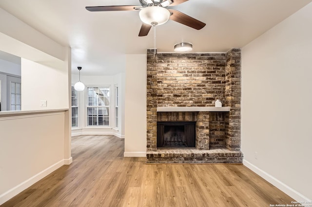 unfurnished living room with wood finished floors, a ceiling fan, a brick fireplace, and baseboards