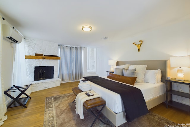 5A Rolling Acres Rd, Boerne, TX 78006 - bedroom with an AC wall unit, wood finished floors, and a stone fireplace