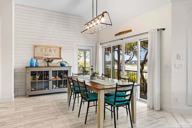 dining area with baseboards, wood finished floors, wooden walls, and high vaulted ceiling