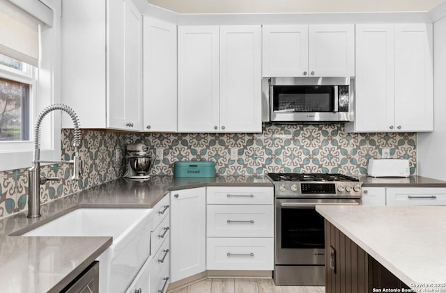 kitchen with appliances with stainless steel finishes, a sink, white cabinets, and backsplash