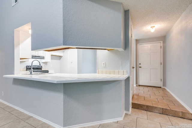 5615 Timber Bark, San Antonio, TX 78250 - kitchen featuring a peninsula, light tile patterned floors, white cabinetry, light countertops, and a textured wall