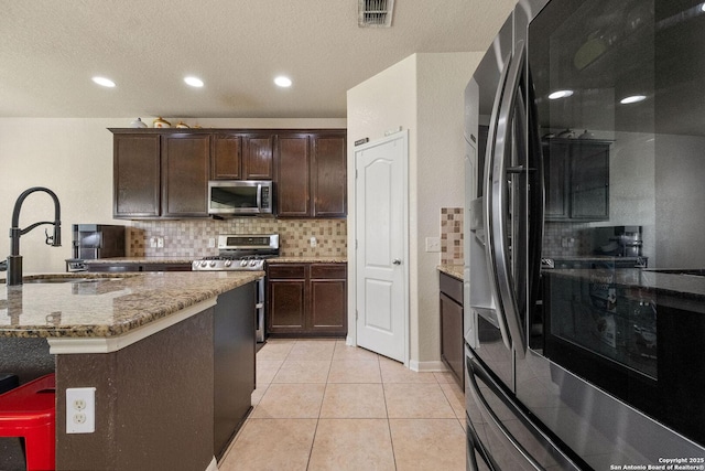 kitchen with a sink, stainless steel appliances, tasteful backsplash, light tile patterned floors, and dark brown cabinetry