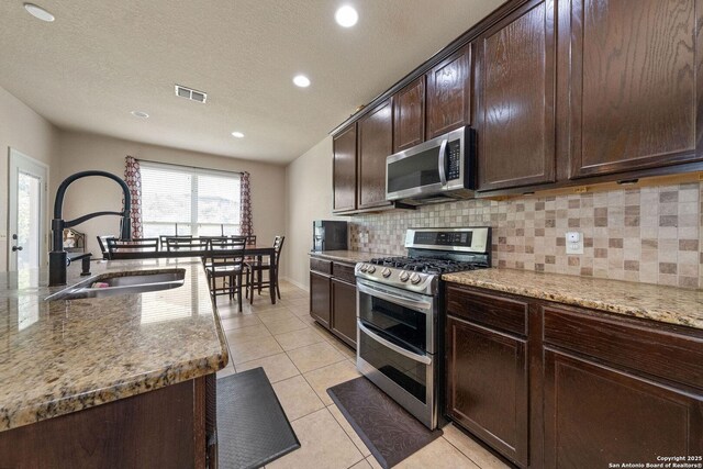 kitchen featuring stainless steel appliances, a sink, backsplash, light stone countertops, and light tile patterned flooring