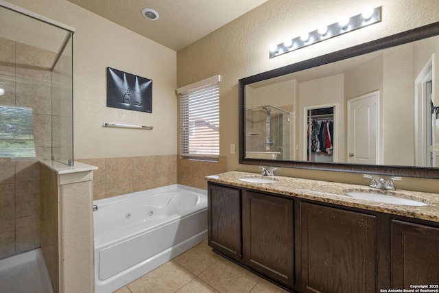 full bath featuring a shower stall, a textured wall, tile patterned floors, a whirlpool tub, and double vanity