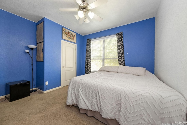 carpeted bedroom featuring baseboards, a ceiling fan, and a textured wall