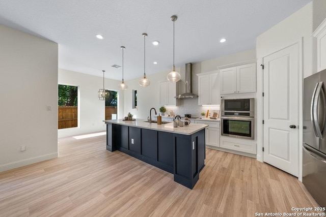 1310 S Mesquite, San Antonio, TX 78210 - kitchen featuring appliances with stainless steel finishes, wall chimney exhaust hood, white cabinetry, light wood finished floors, and a sink