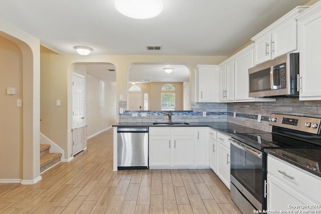 kitchen with appliances with stainless steel finishes, a sink, arched walkways, and backsplash