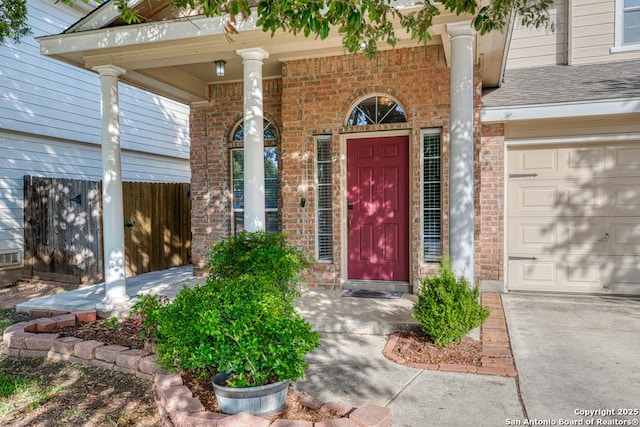 view of exterior entry featuring brick siding, a garage, and covered porch