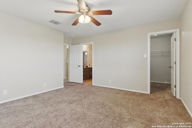 unfurnished bedroom with light colored carpet, a spacious closet, baseboards, a closet, and ensuite bathroom