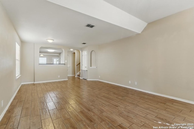 spare room with arched walkways, wood finished floors, baseboards, and stairs