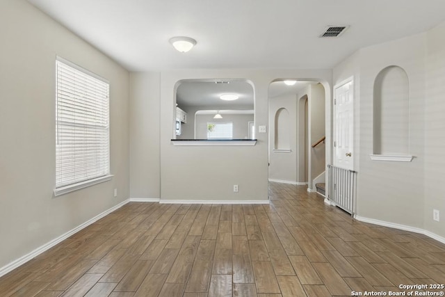 empty room featuring wood finished floors, arched walkways, baseboards, and stairway