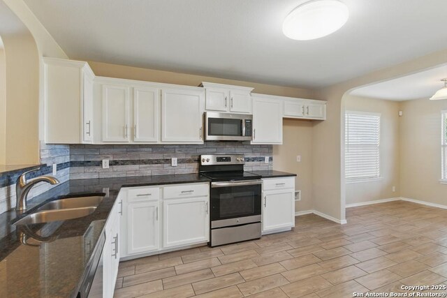 kitchen featuring appliances with stainless steel finishes, a sink, arched walkways, backsplash, and white cabinets