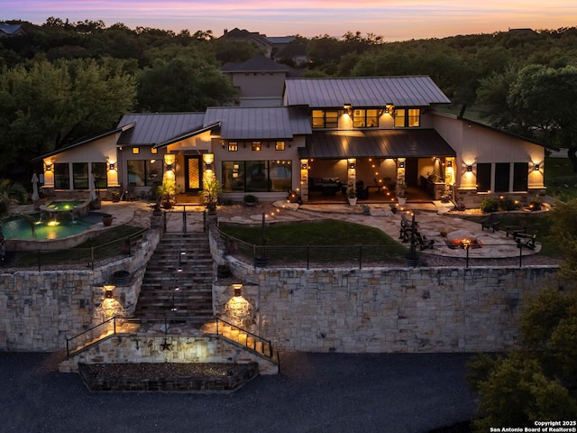 back of property at dusk with a patio area, stairs, fence, an in-ground hot tub, and metal roof