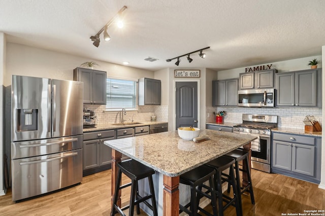 kitchen featuring appliances with stainless steel finishes, a sink, gray cabinetry, track lighting, and a textured ceiling