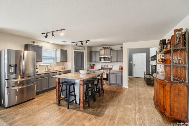 kitchen with appliances with stainless steel finishes, gray cabinets, a sink, a breakfast bar area, and wood finished floors
