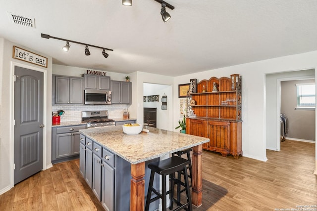 kitchen with appliances with stainless steel finishes, gray cabinets, rail lighting, tasteful backsplash, and light wood finished floors