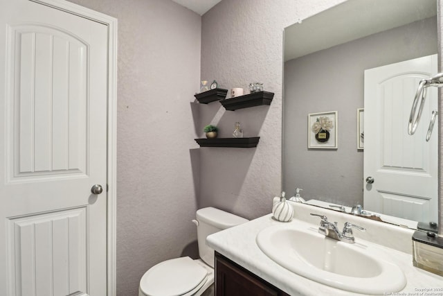 half bath with toilet, a textured wall, and vanity