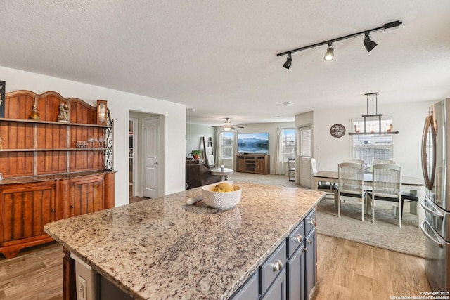 kitchen featuring freestanding refrigerator, light wood-style floors, a ceiling fan, light stone counters, and a textured ceiling