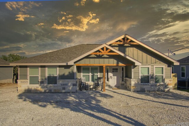 1139 Cedar Bnd, Canyon Lake, TX 78133 - back of house at dusk with board and batten siding, central AC unit, roof with shingles, and stone siding