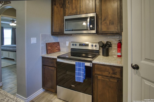 1139 Cedar Bnd, Canyon Lake, TX 78133 - kitchen featuring appliances with stainless steel finishes, tasteful backsplash, arched walkways, light wood-type flooring, and light stone counters